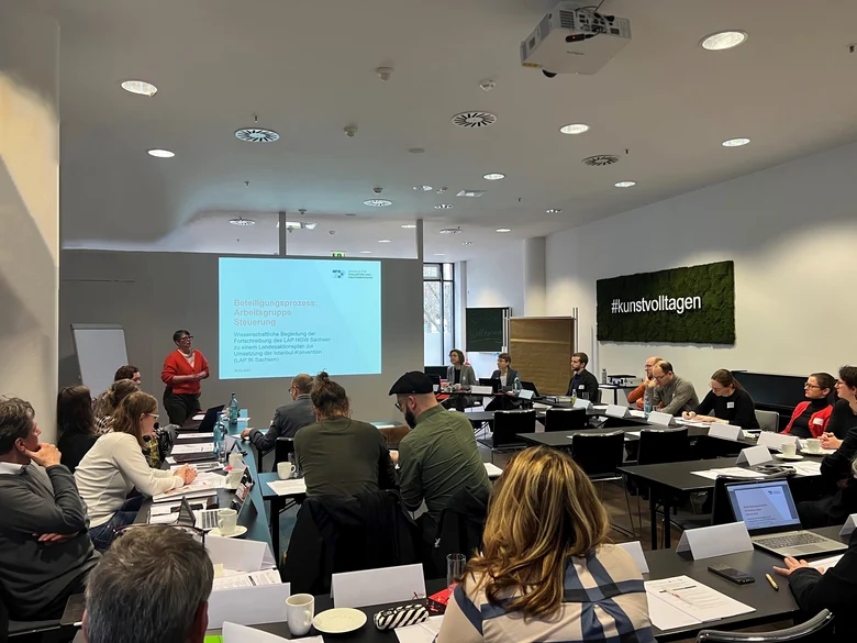 viele Menschen sitzen auf Stühlen an Tischen und arbeiten zusammen