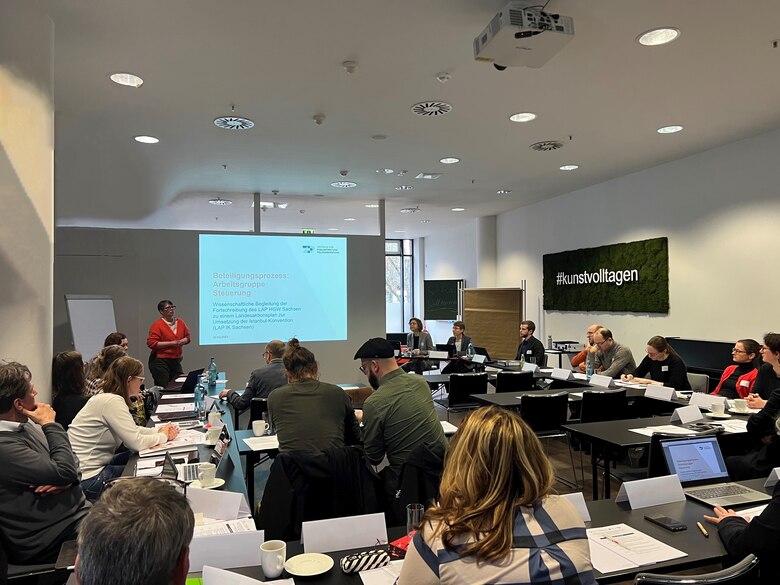 viele Menschen sitzen auf Stühlen an Tischen und arbeiten zusammen