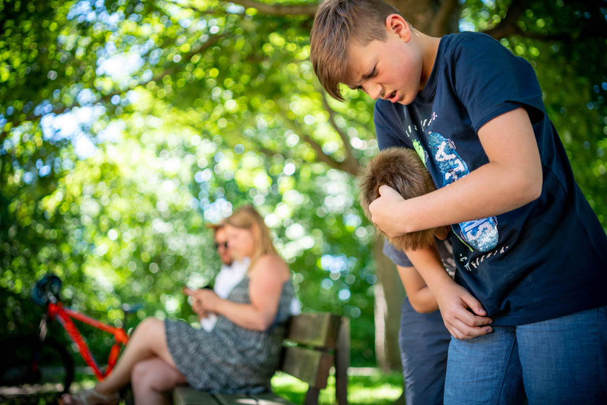 Zustimmendes Verhalten von Eltern zur Gewalt unter Kindern. Eltern sitzen auf Parkbank mit Handys und Kinder prügeln sich ohen einzugreifen.