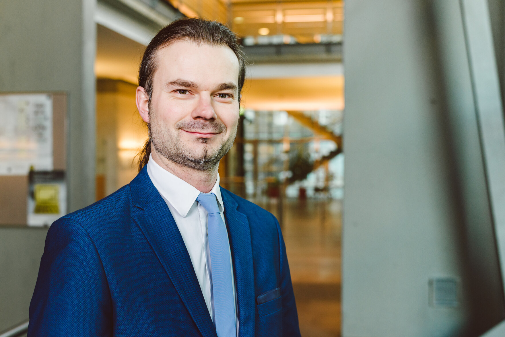 Foto im Querformat, Herr Forkert in Portraitansicht mit weißem Hemd, blauem Jacket und hellblauem Schlips im Foyer des SMI