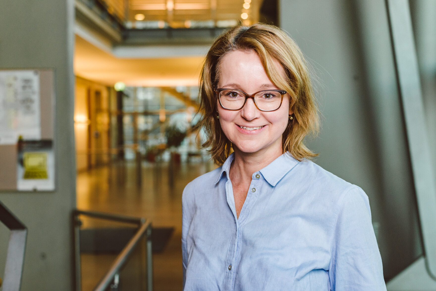 Foto im Querformat, Elke Medina in Portraitansicht mit heller Bluse und im Hintergrund das Foyer des SMI