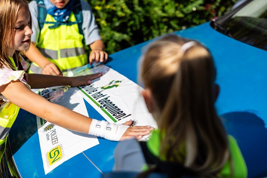 Kinder bekleben die Motorhaube des Polizeiautos mit Die Schule hat begonnen.