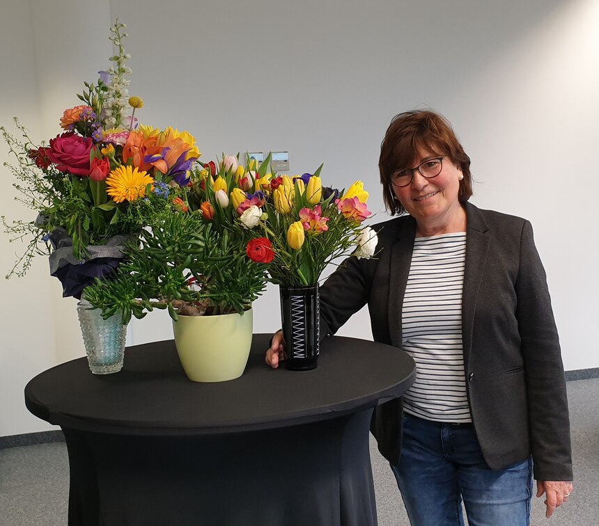 Portraitfoto von Frau Kynast neben einem Stehtisch mit Blumenstrauß