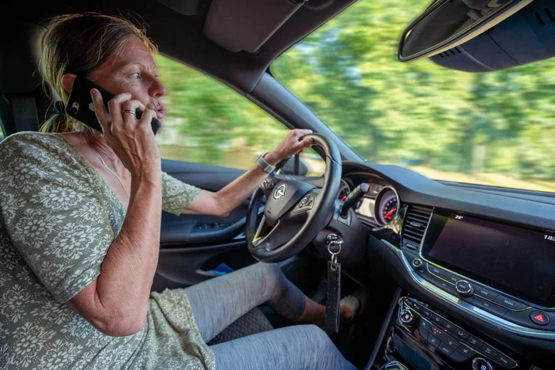 eine Frau sitzt hinter dem Lenkrad eines Autos und hält dabei ein Telefon an ihr rechtes Ohr.