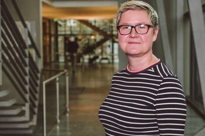 Doreen hat blonde kurze Haare und trägt eine Brille. Außerdem trägt sie ein schwarz weiß gestreiftes langarm-T-Shirt