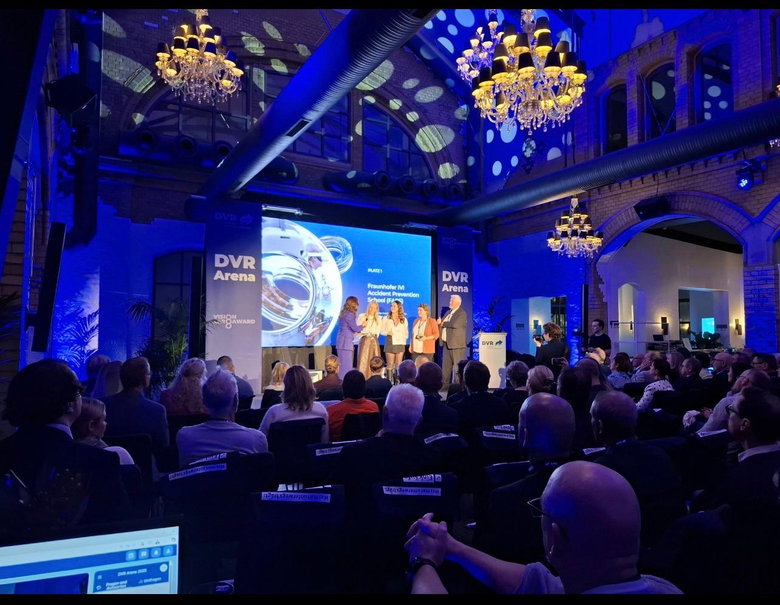 Viele Menschen sitzen auf Stühlen und schauen zur Bühne vor, auf dieser stehen vier Personen, denen ein Preis der Vision Zero Award des Deutschen Verkehrssicherheitsrates ausgehändigt wird.