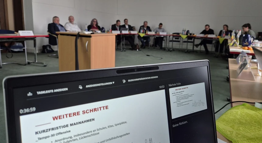 ein Ausschnitt von einem Laptop-Bildschirm dahinter verschwommen Personen die an einem Tisch auf Stühlen sitzen