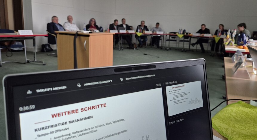 ein Ausschnitt von einem Laptop-Bildschirm dahinter verschwommen Personen die an einem Tisch auf Stühlen sitzen