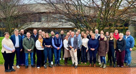 viele Personen stehen auf der Wiese vor einem Gebäude und schauen in die Kamera für ein Gruppenbild