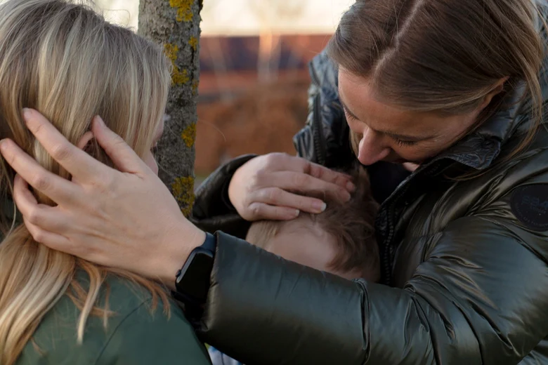 eine Mutter mit zwei Kindern in einem Park, die schützend die Hände über die Kinder legt