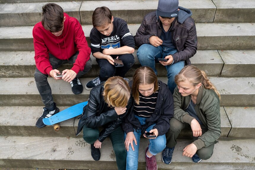 Mehrere Kinder und Jugendliche sitzen auf Treppenstufen und schauen auf ihre Handys, die sie jeweils in den Händen halten.