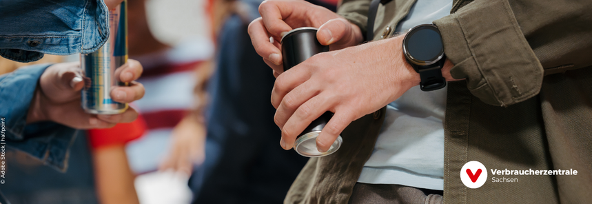Dosen mit Energydrink die in den Händen gehalten werden, im Hintergrund verschwommen die Umrisse von Personen