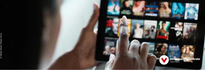 verschwommen ein Desktop mit verschiedenen Filmangeboten, davor sitzt eine Person, die mit dem Finger symbolisch einen Film anklickt