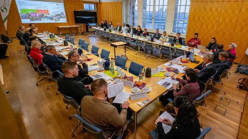 Menschen sitzen in Konferenzbestuhlung in einem Raum und schauen nach vorn zu einer Präsentation