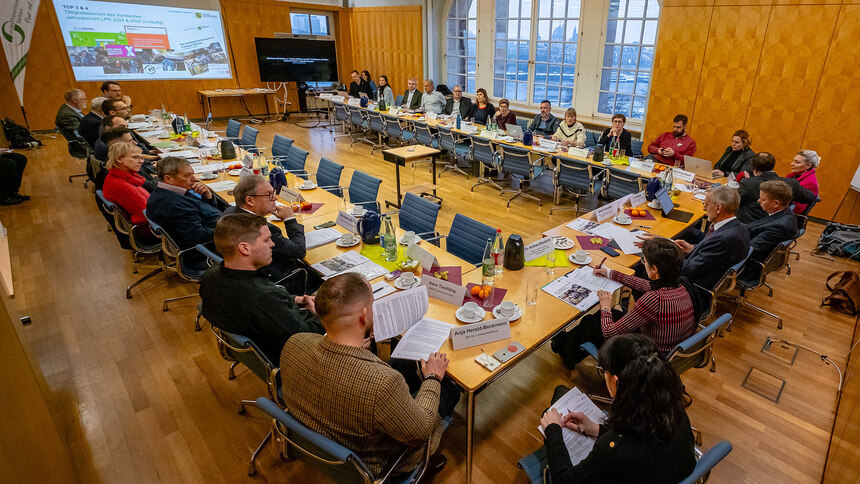 Menschen sitzen in Konferenzbestuhlung in einem Raum und schauen nach vorn zu einer Präsentation