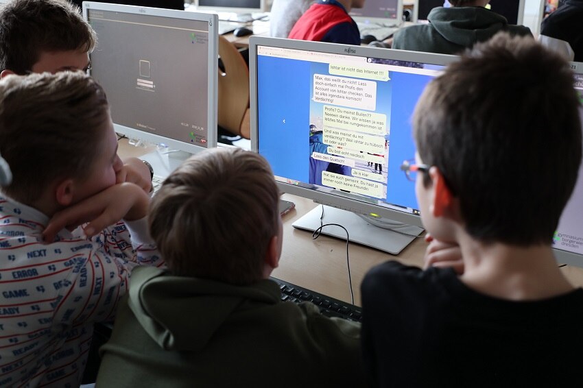 vier Jungs der 7. Klasse schauen auf einen Computerbildschirm und diskutieren über Hate Speech und wie man sich dagegen wehren kann.