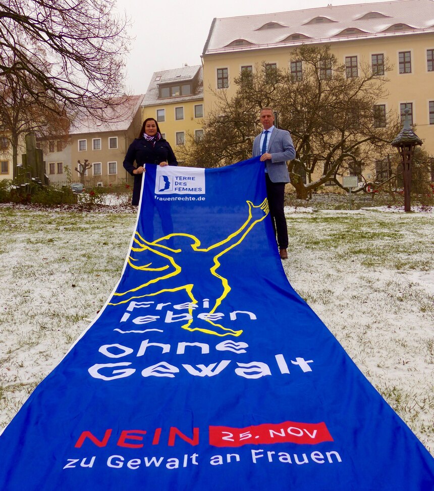 Bild zeigt Bürgermeister der Stadt Stolpen sowie Gleichstellungsbeauftrage Sophie Knuth mit der Fahne zum Internationalen Tag gegen Gewalt an Frauen