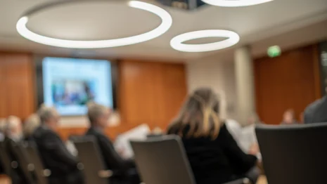 unscharfes Bild eines Konferenzraums, im Hintergrund mehrere Personen an einem Tisch sitzend