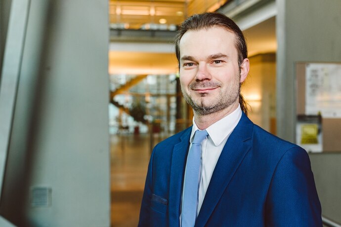 Sven Forkert trägt braune Haare und einen Bart. Er hat ein schwarzes Hemd und ein blaues Jackett an.