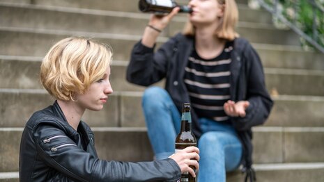 zwei Mädchen sitzen auf eine Treppe und trinken Bier.