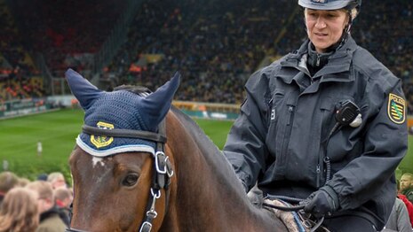 Rückansicht eines Einsatzbeamten der Polizei, davor zahlreiche Fußballfans die in die Schuttle-Busse einsteigen. 