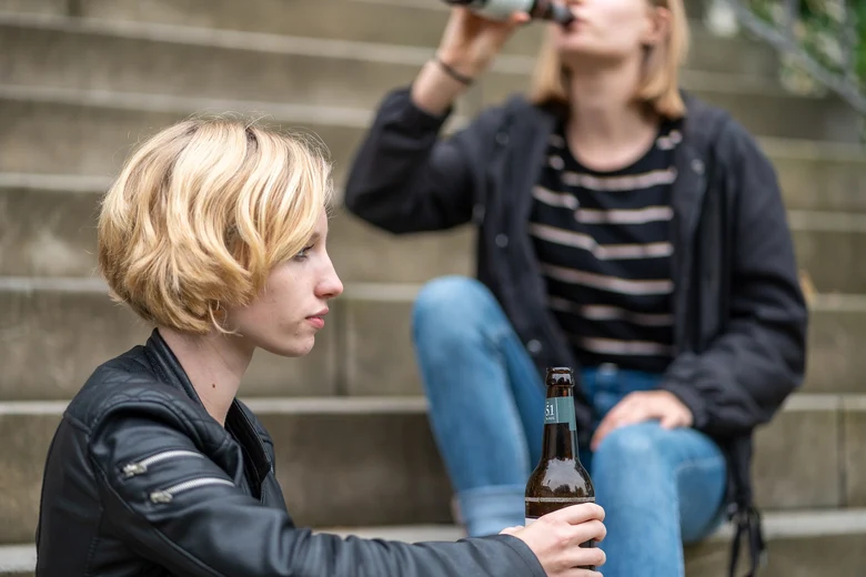 zwei junge Mädchen sitzen versetzt auf Treppenstufen und konsumieren Alkohol