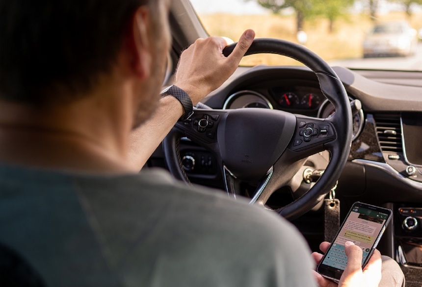 Autofahrer hinter dem Steuer mit einem Handy in der Hand