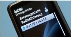 Ein Ausschnitt eines Mobiltelefons. Die Nummer der »Beratungsstelle Radikalisierung« ist auf dem Display als Kontakt eingespeichert und hell erleuchtetet.
