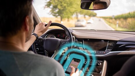 Autofahrer tippt während der Fahrt etwas in sein Smartphone und es ist Gegenverkehr durch die Frontscheibe zu sehen